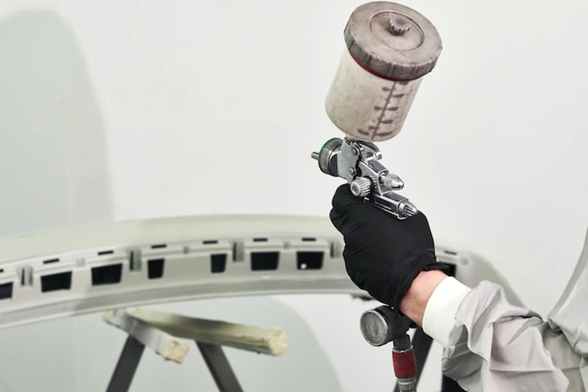 Mechanik malujący zderzak samochodu w kabinie malarskiej