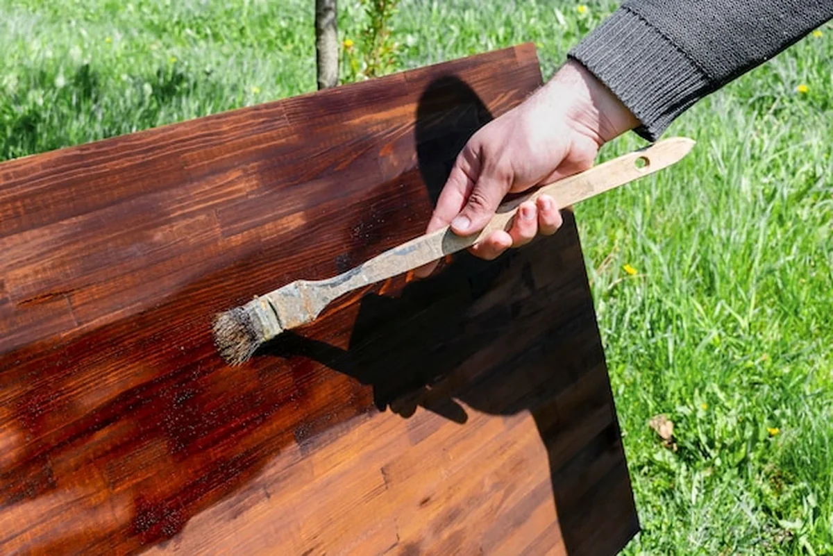 Mężczyzna maluje drewno pędzlem na drewnianym stole