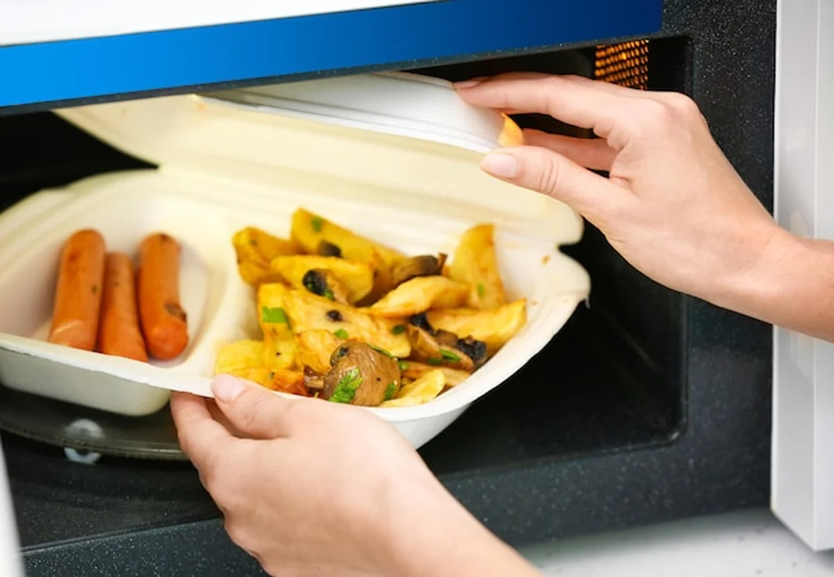 Kobieta wkładająca plastikowy pojemnik do mikrofalówki