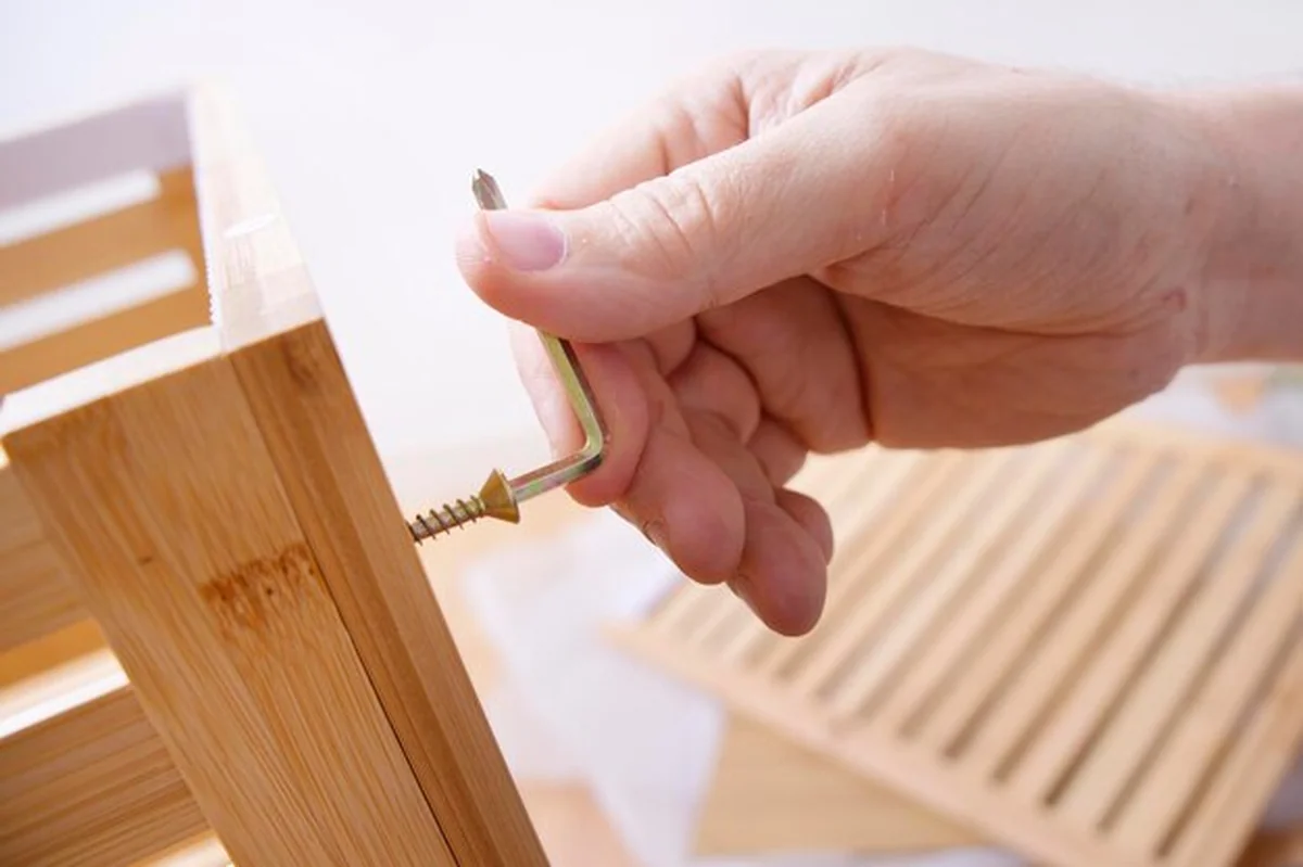 Stolarz dokręca śrubę kluczem imbusowym na drewnianym meblu
