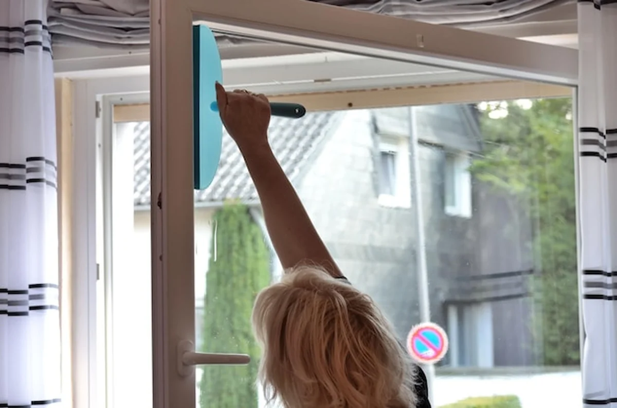 Kobieta sprzątająca okno z skrobakiem w domu