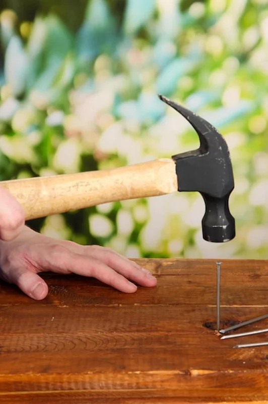 Budowniczy wbijający gwoździe w deskę na tle natury