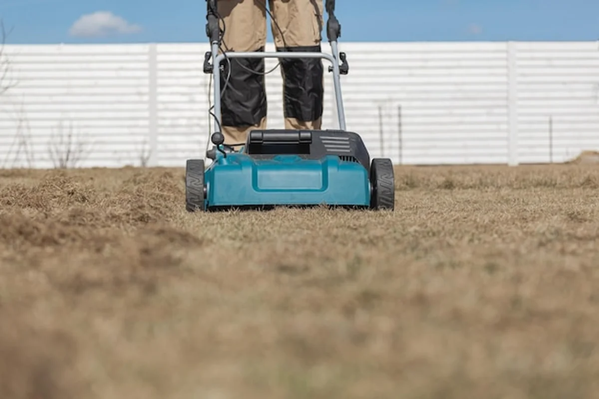 Mężczyzna ogrodnik wertykuluje trawnik przy użyciu wertykulatora