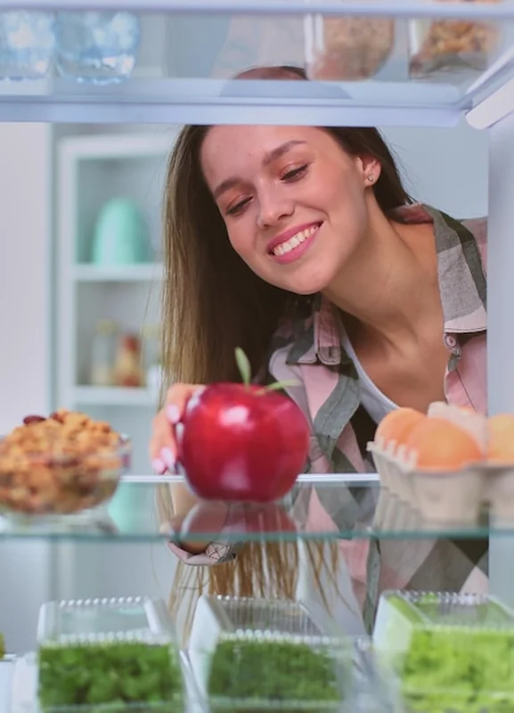 Kobieta przy otwartej lodówce pełnej warzyw i owoców