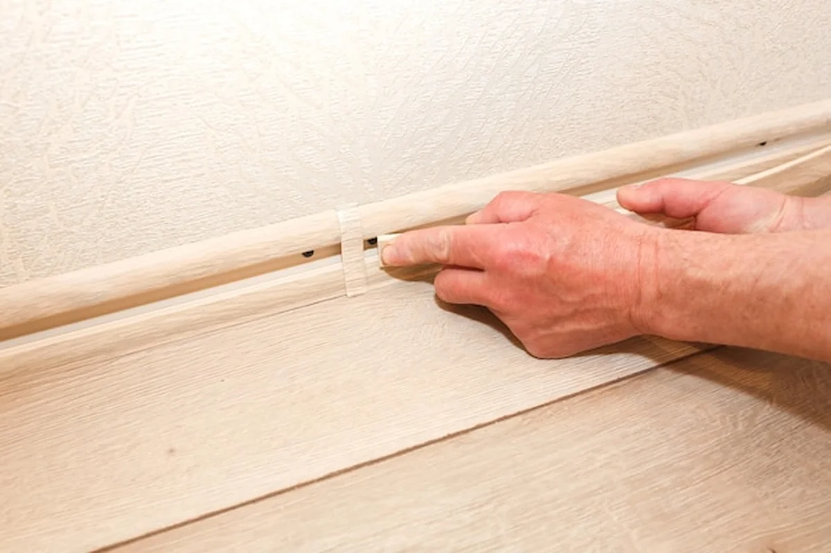 Mężczyzna montuje listwę przypodłogową podczas prac naprawczych w mieszkaniu