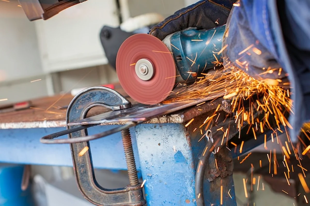 Szlifowanie metalu na stalowej płycie z błyskiem iskier z bliska nosić rękawice ochronne