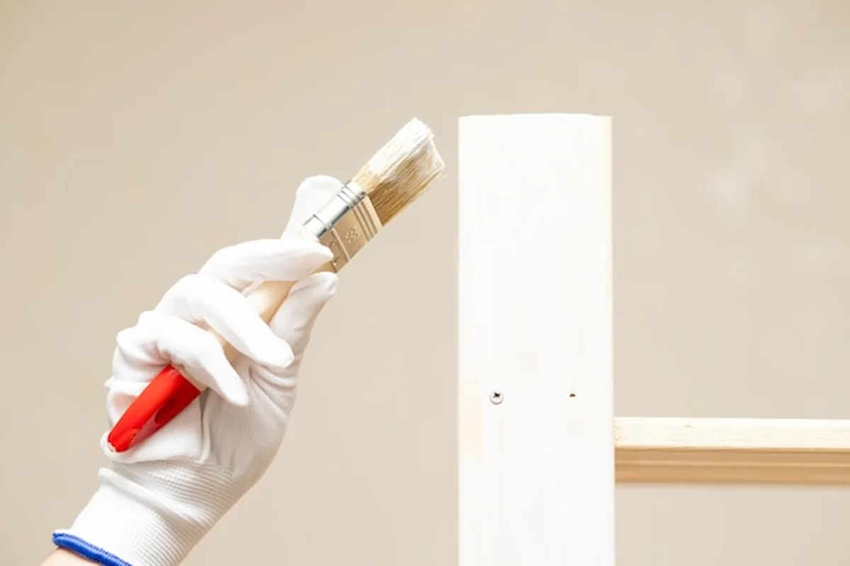 Dłonie w rękawiczkach malują drewniane meble pędzlem