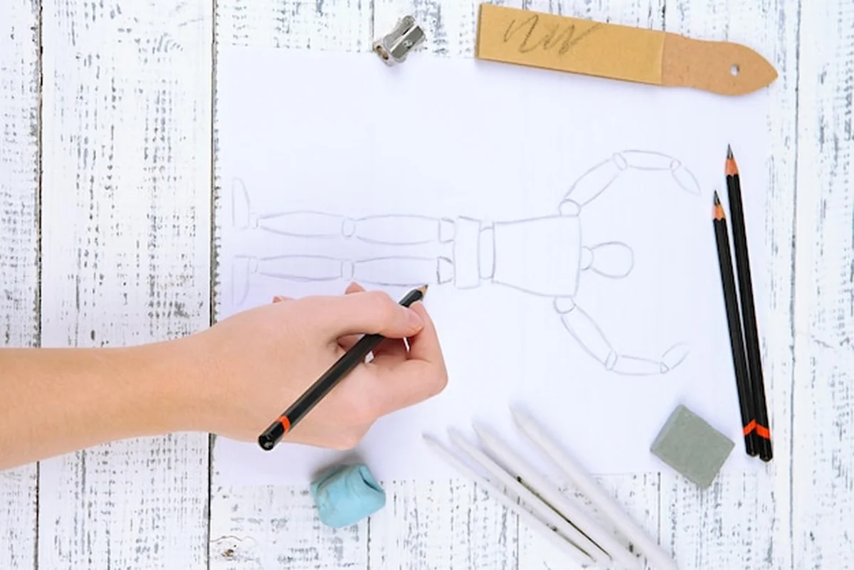 Ręka rysuje szkic z profesjonalnymi materiałami artystycznymi na drewnianym stole