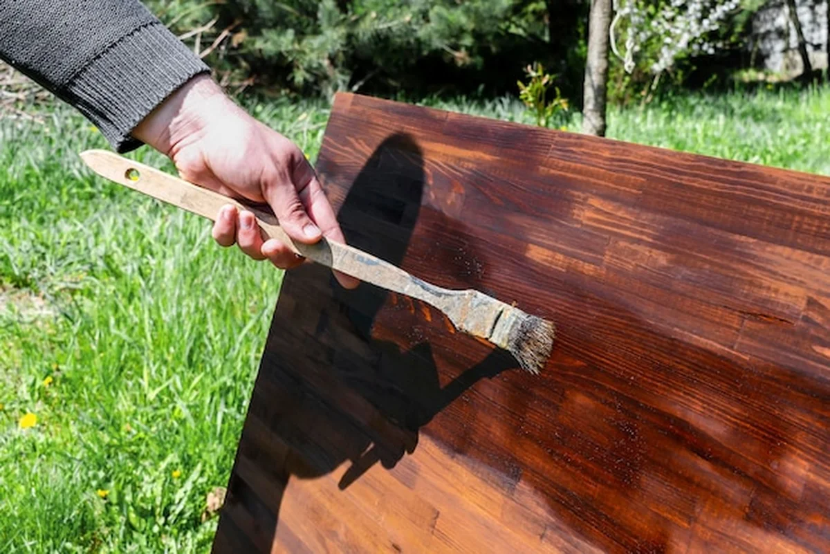 Mężczyzna maluje drewniany stół brązową plamą olejną