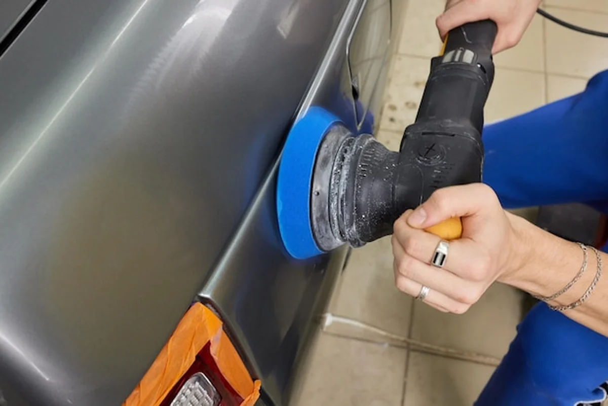 Ręce z polerką orbitalną na detalach samochodu w warsztacie samochodowym