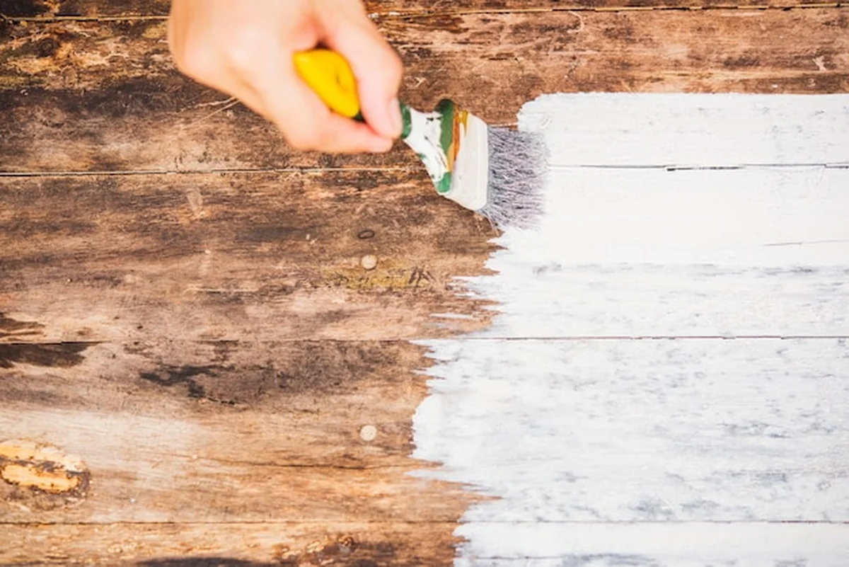 Ręka kobiety maluje stare drewno pędzlem na biało