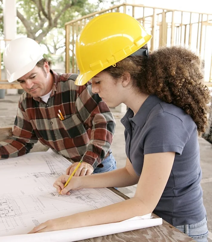 Studentka inżynierii na placu budowy z planami, obok instruktora