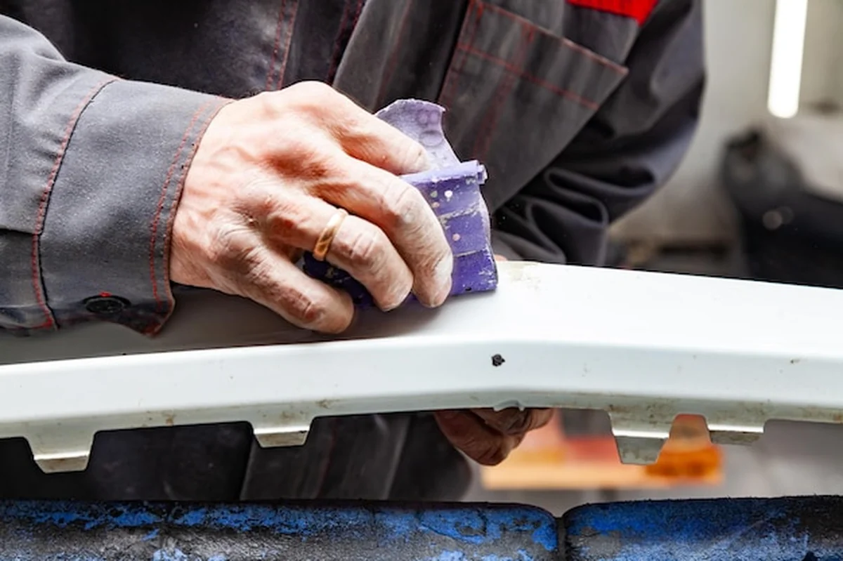 Mężczyzna przygotowuje element karoserii do malowania po wypadku w warsztacie samochodowym