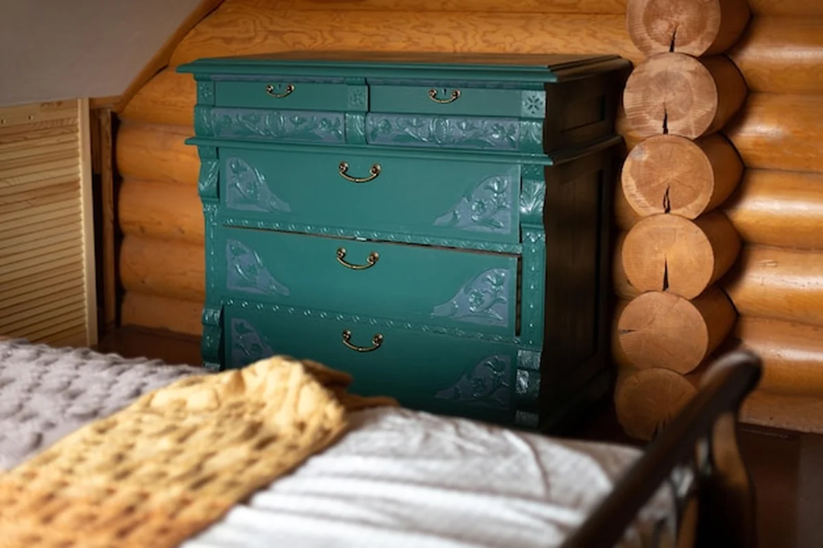 Stara, turkusowa komoda pod podwójnym drewnianym łóżkiem w wiejskim domu