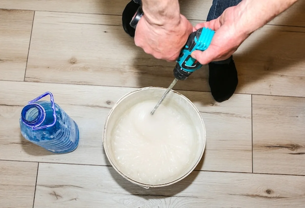 Mężczyzna miesza gęsty klej w wiadrze przy tapetowaniu