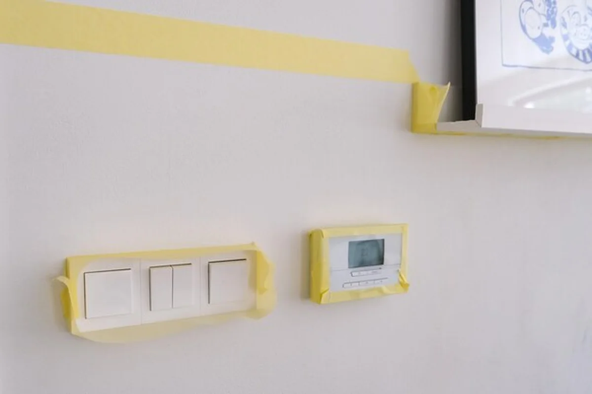 Przygotowanie malowania ścian taśmą maskującą na termostatach, przełącznikach, meblach