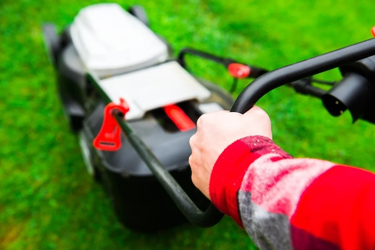 Mężczyzna trzyma kosiarkę na zielonej trawie przed domem