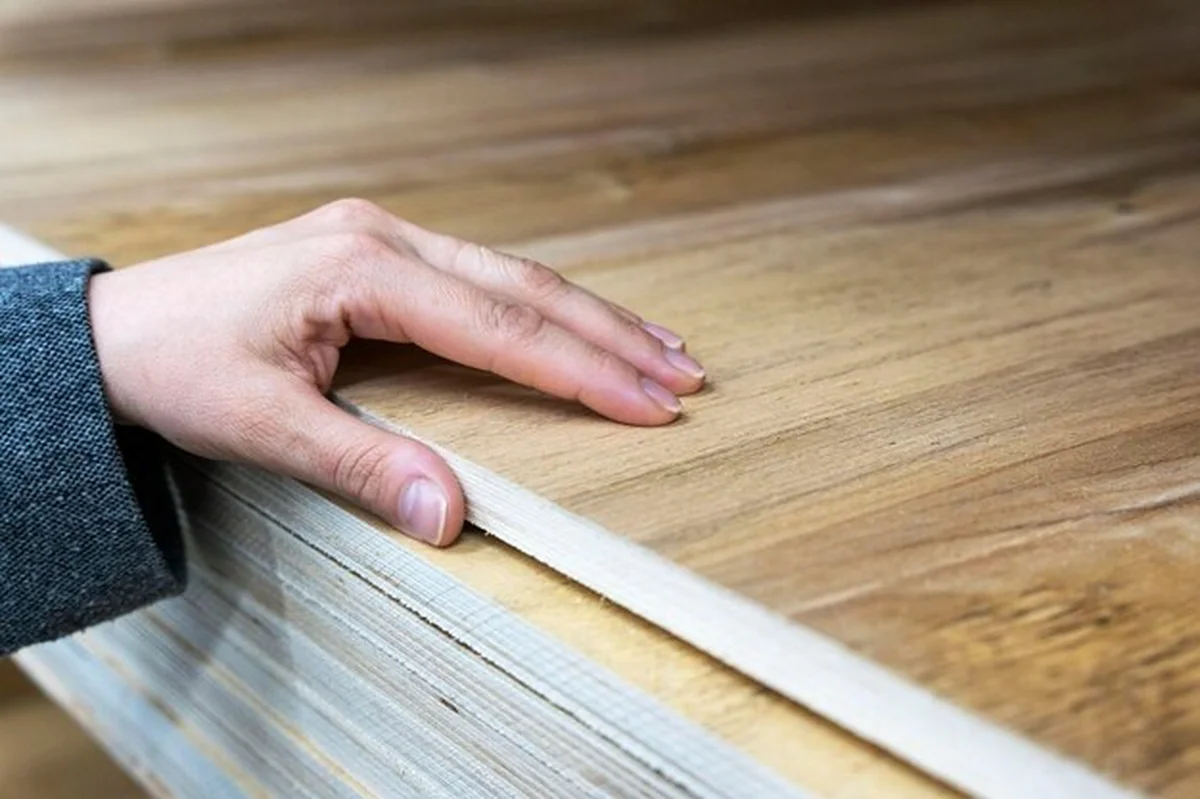 Ręka kupującego wybiera gruby arkusz sklejki laminowanej w sklepie