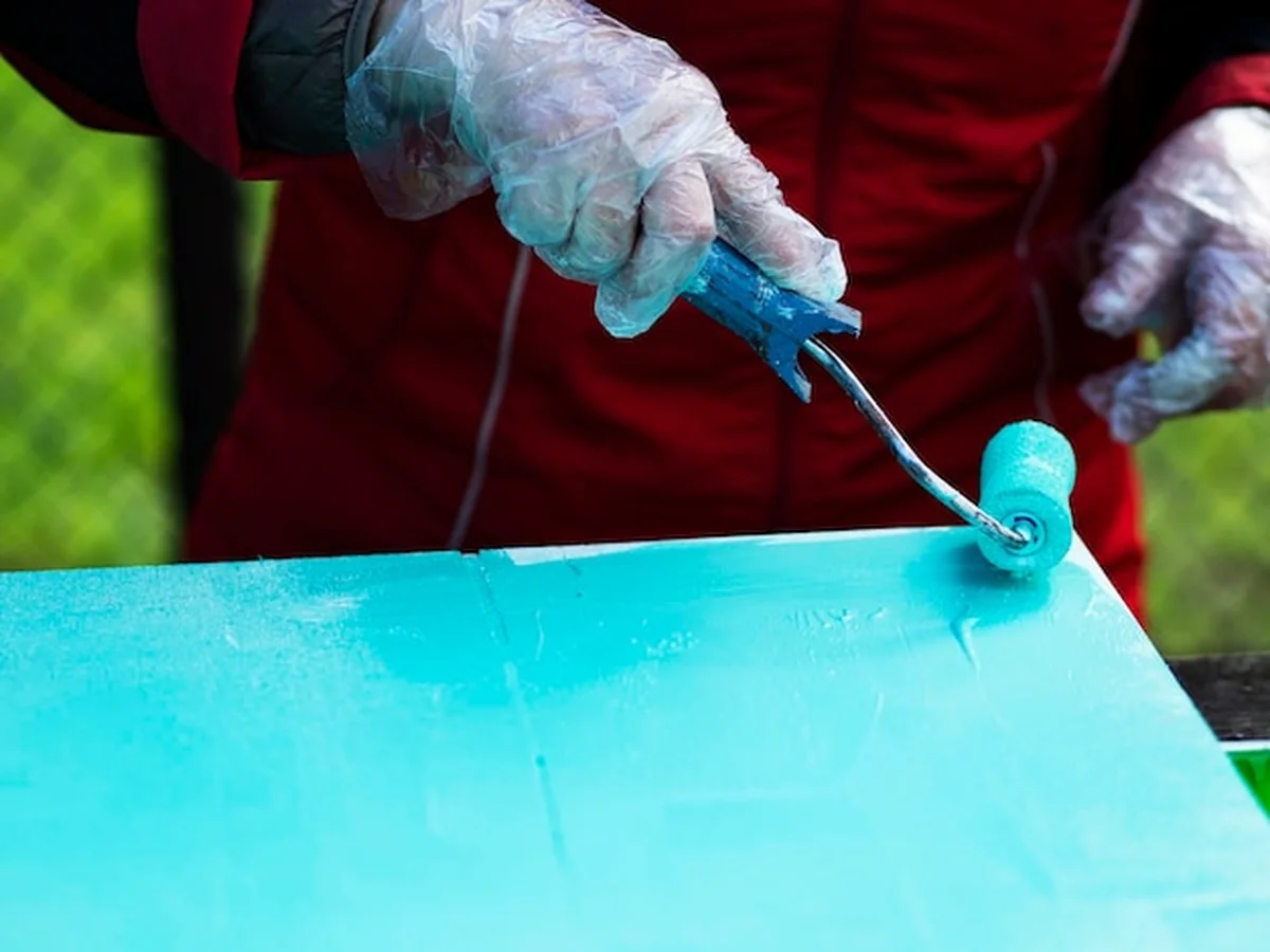 Ręka kobiety maluje arkusz sklejki turkusową farbą za pomocą rolki