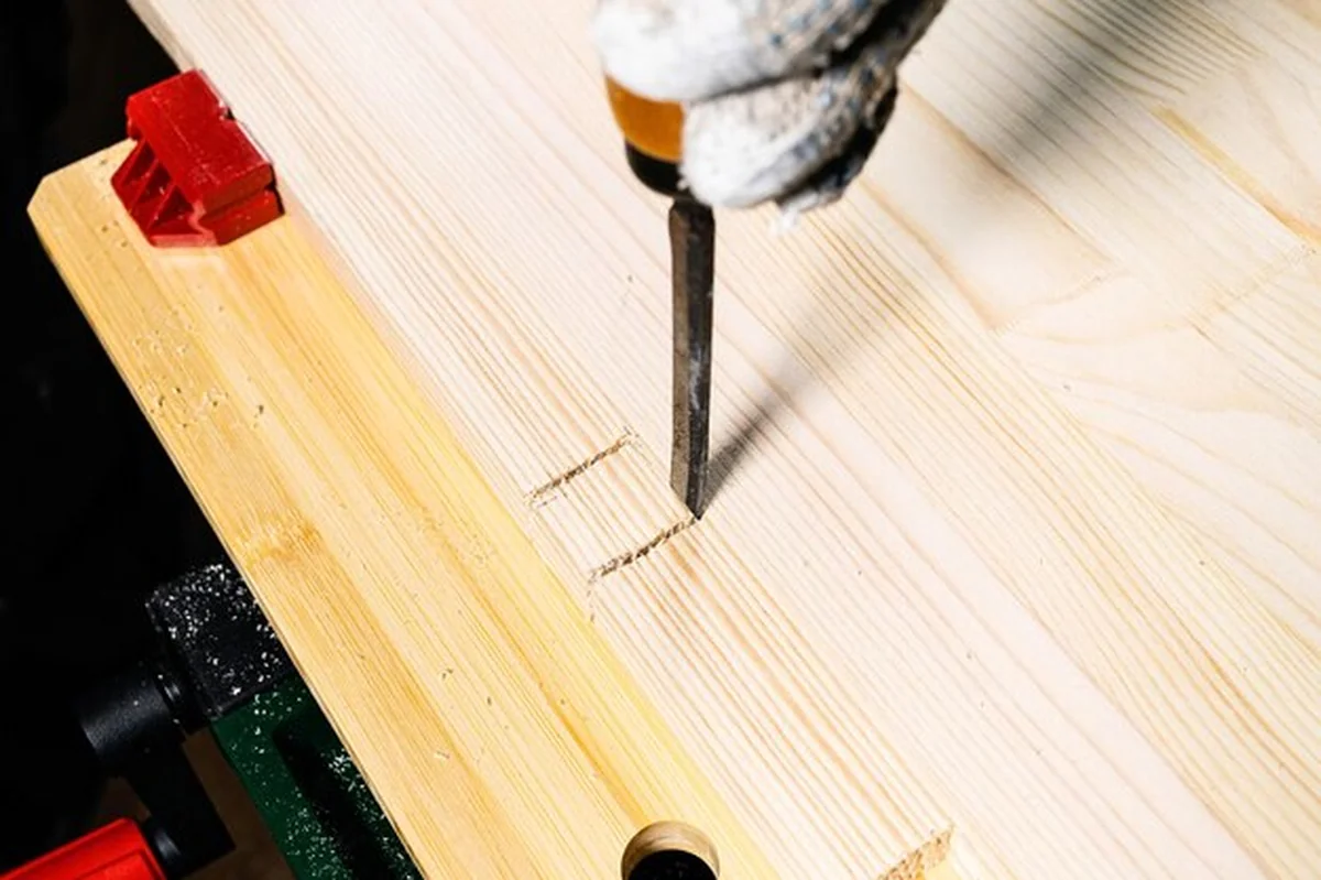 Stolarz za pomocą dłuta wycina szczelinę na drewnianej desce