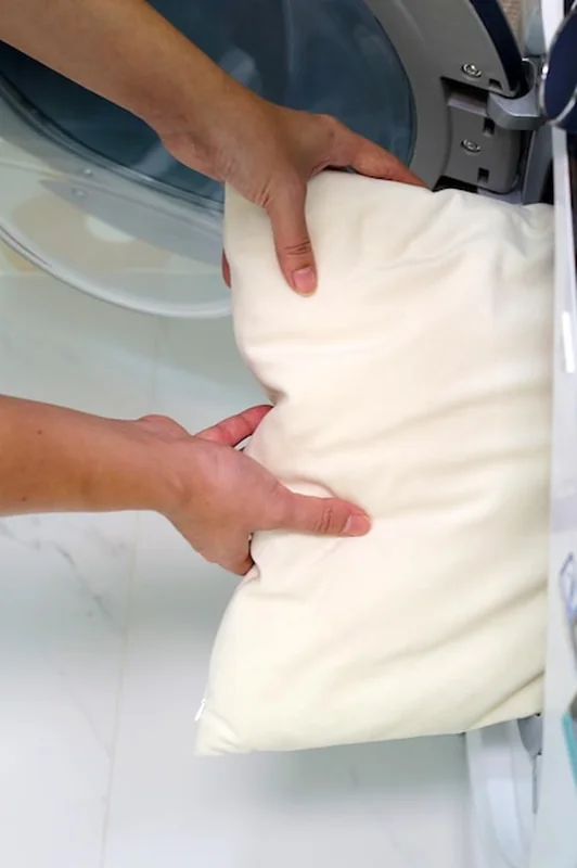 Ręka mężczyzny wkłada poduszkę do pralki