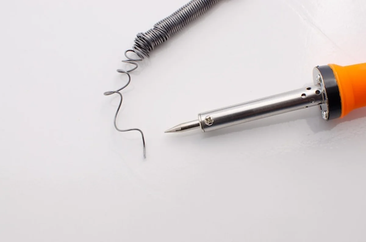 Lutownica elektryczna z pastą lutowniczą i drutem na białej powierzchni