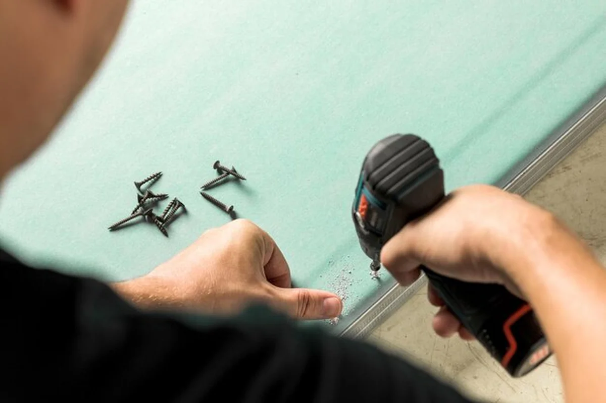 Budowniczy wkręca śrubę w płytę gipsowo-kartonową