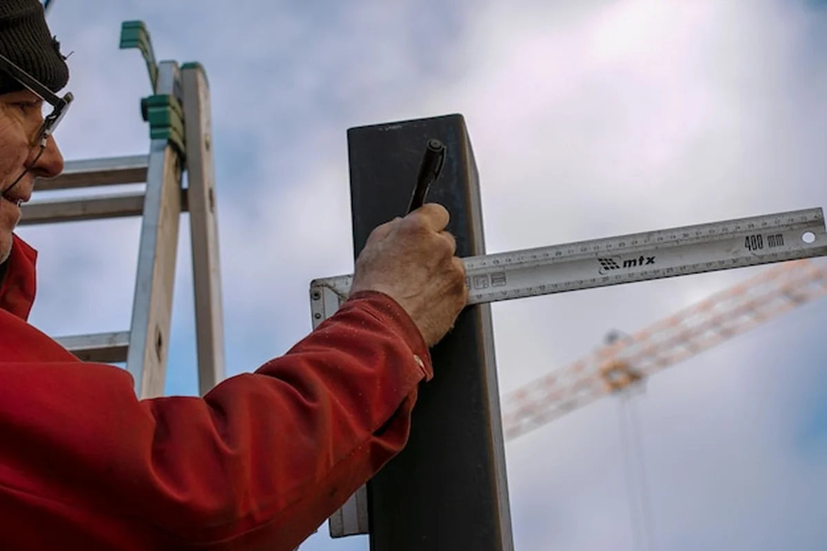 Robotnik mierzy linie na rurze żelazną linijką